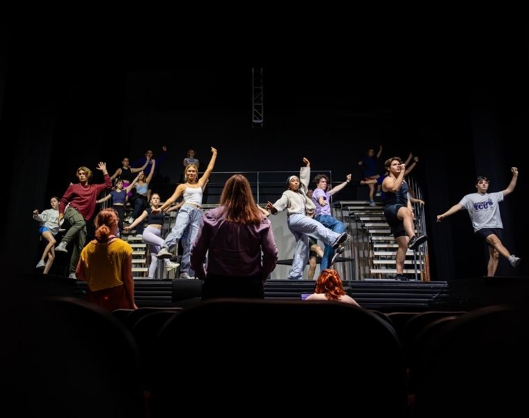 TCU Theatre students rehearse a dance number onstage, performing choreography across a multilevel set.